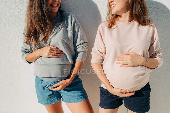 Две беременные женщины держатся за живот и улыбаются друг другу. — стоковое фото