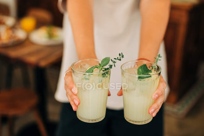 Mains féminines tenant deux verres de limonade froide avec menthe et glace — Photo de stock