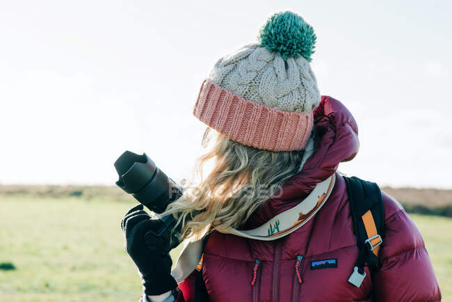 Mujer sosteniendo una cámara réflex digital mirando hacia el sol en invierno - foto de stock