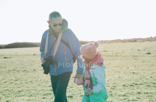 Abuelo sosteniendo la mano de su nieta mientras camina al aire libre - foto de stock
