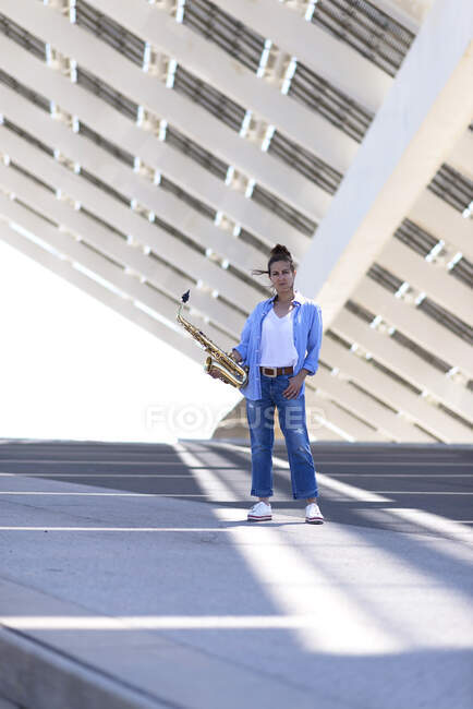 Femme avec queue de cheval debout tout en posant avec un saxophone à l'extérieur — Photo de stock