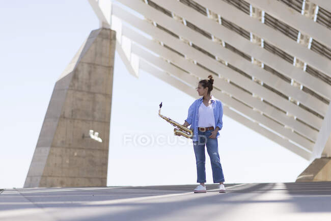Woman with ponytail standing while posing with a saxophone outdoors — Stock Photo