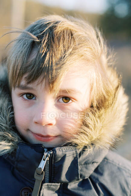 Petit garçon gelé souriant au coucher du soleil en hiver avec un manteau épais — Photo de stock