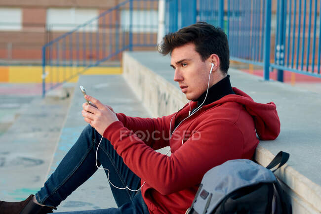 Student man holds his mobile and listen to music in a basketball — Stock Photo