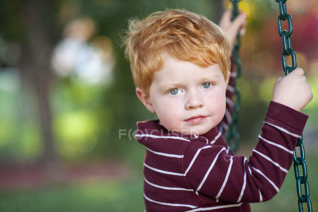 Close up of young boy 3-4 years old swinging on tire swing outdoors — Stock Photo