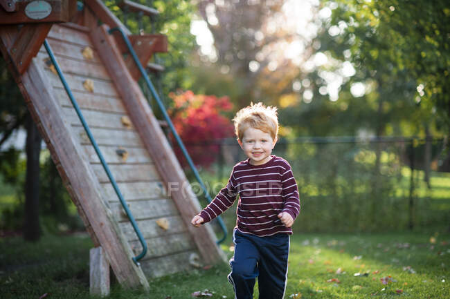 Jovem rapaz 3-4 anos correndo através da grama no quintal durante o outono — Fotografia de Stock