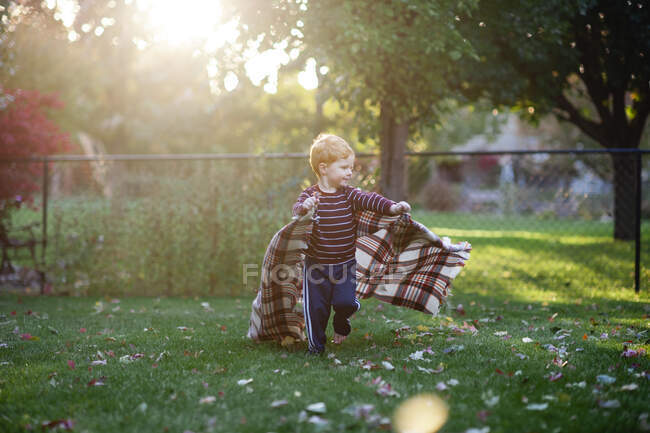 Boy 3-4 years old running backyard with blanket in pretty light — Stock Photo