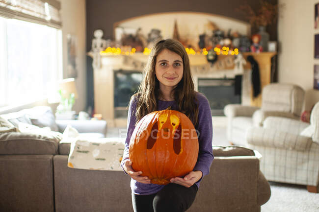 Tween girl 10-12 years old holds up carved pumpkin in living room — Stock Photo