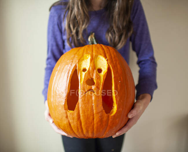 Close up of tween girl holding up carved pumpkin of dog against wall — Stock Photo