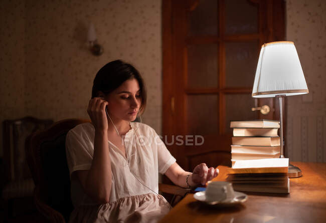 Young female putting on earphones and browsing mobile phone while reading books — Stock Photo