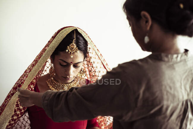 Las mujeres jóvenes ayudan a la novia india a preparar el vestido tradicional para la boda - foto de stock