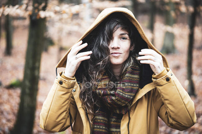 Young woman with curly long hair smiles in warm winter coat in forrest — Stock Photo