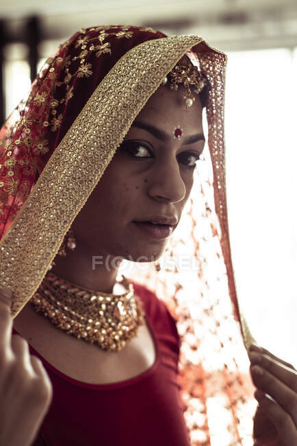 Giovane donna indiana tira sul velo rosso matrimonio in luce finestra — Foto stock