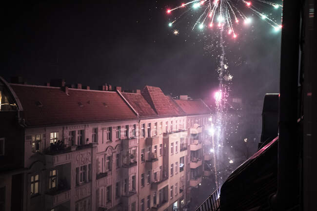 Coloridos fuegos artificiales estallan desde el balcón vista de la calle en la ciudad de Berlín - foto de stock