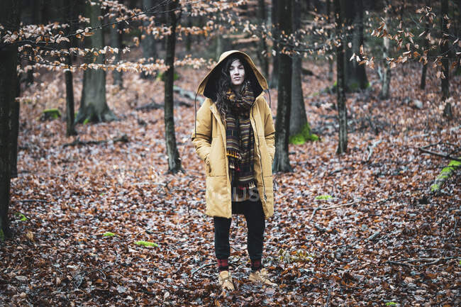 Natural strong woman with winter coat and scarf stands in golden woods — Stock Photo