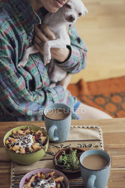 Persona coccola cane cucciolo carino a tavola con colazione sana e caffè — Foto stock
