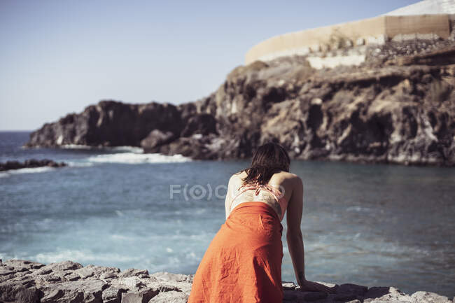 Strong fit woman in swimsuit leans on stone wall looking down to ocean — Stock Photo