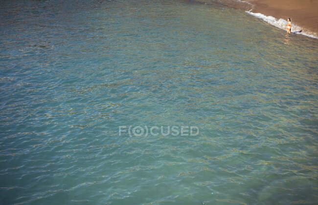 Mujer se para en la costa sola mirando hacia fuera a la vasta agua azul del océano - foto de stock
