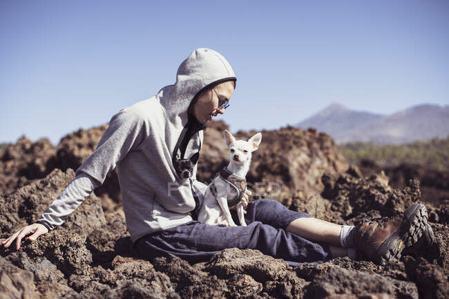 Senderista saludable lados en piedra volcánica en las montañas con perros chihuahua - foto de stock