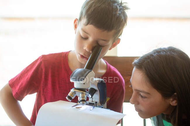 Хлопчик дивиться у мікроскоп з дівчиною, яка дивиться на — стокове фото