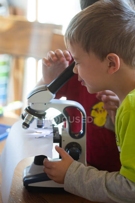 Маленький мальчик смотрит в микроскоп дома — стоковое фото