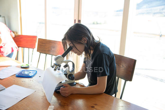 Девочка на домашнем обучении смотрит под микроскопом — стоковое фото