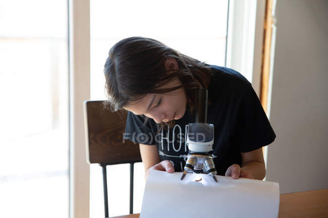 Девушка смотрит на жука под микроскопом за кухонным столом — стоковое фото