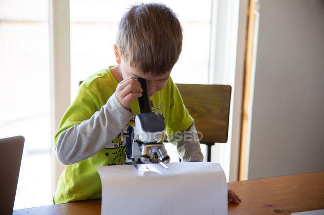 Хлопчик працює над науковим експериментом з мікроскопом — стокове фото