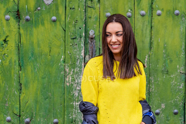 Портрет молодої жінки, яка посміхається, стоячи на відкритому повітрі навпроти зелених старих дверей. Подорожі та міська концепція . — стокове фото