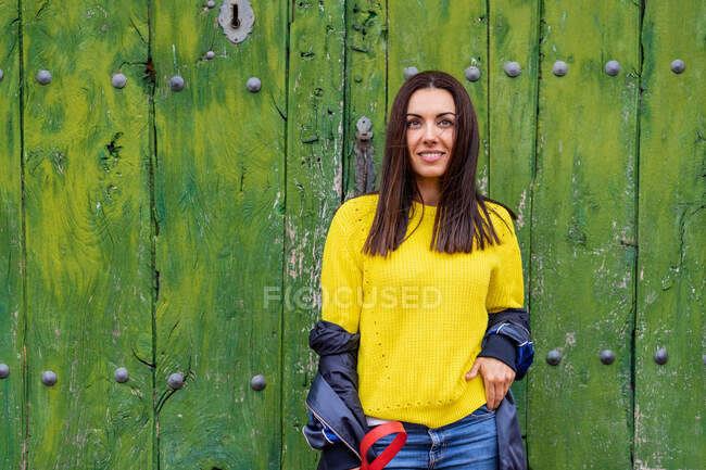 Portrait of woman on a background of a green door with a yellow sweater — Stock Photo