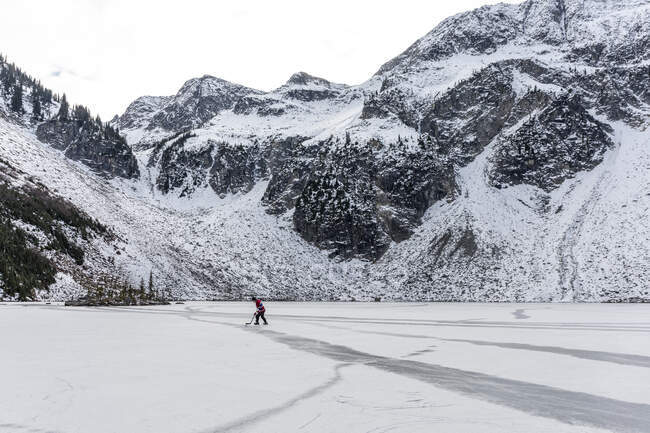 Homem jogando hóquei perto de montanhas nevadas em lago congelado — Fotografia de Stock