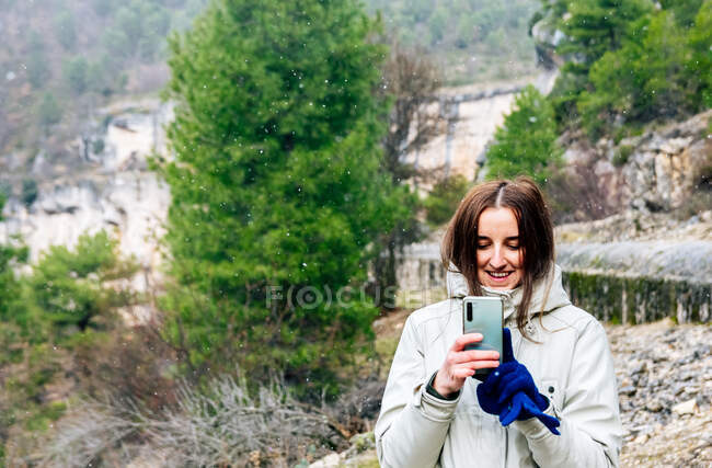 Жінка на горі насолоджується падаючим снігом, використовуючи свій мобільний телефон . — стокове фото
