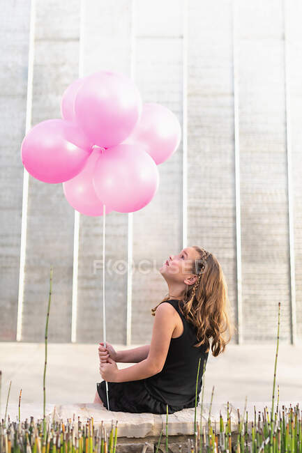A young girl with red balloons and white roses in front of a beautiful park — Stock Photo