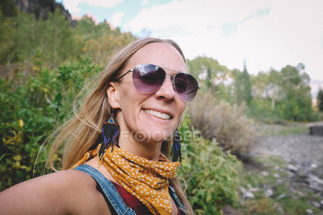 Mujer rubia feliz en gafas de sol se hace selfie en una caminata - foto de stock