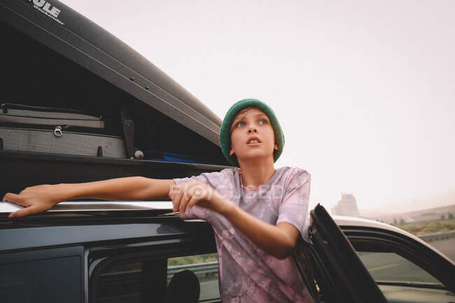 Ragazzo in berretto controlla il bagagliaio in un viaggio su strada. — Foto stock