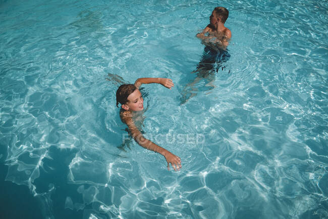 Hermanos nadando en una piscina cristalina - foto de stock