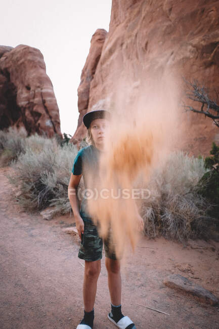 Хлопчик кидає пісок у повітря, оточений пісковиком і пустелею — стокове фото