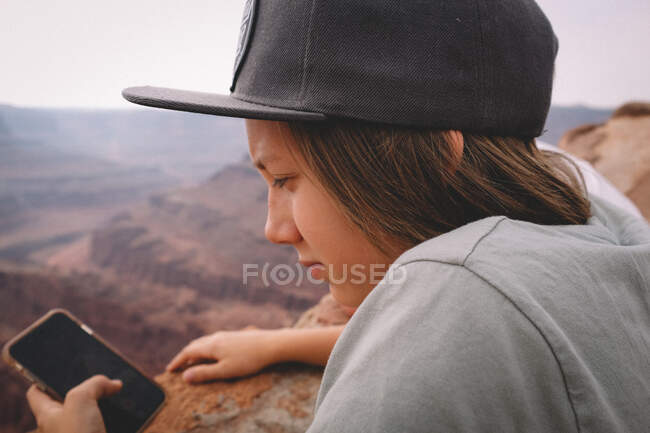 Rapaz a verificar o telemóvel com vista para o desfiladeiro — Fotografia de Stock