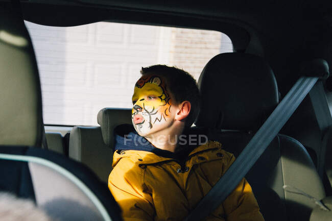 Niño con la cara pintada mirando a la ventana - foto de stock