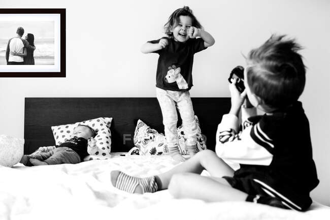 Kids playing with camera and jumping on a bed — Stock Photo