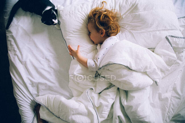 Menina deitada em uma cama e brincando com seu gato — Fotografia de Stock