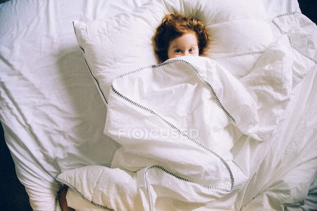 Girl laying in bed with white linens — Stock Photo