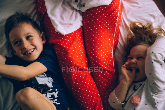 Mamá jugando con hijo e hija en una cama - foto de stock