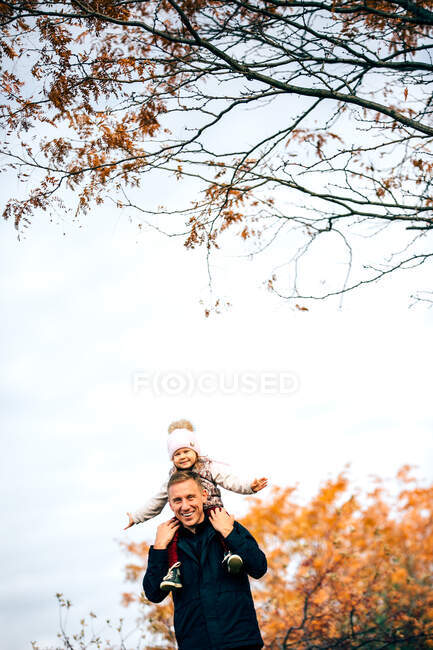 Мужчина держит свою дочь и стоит под деревом — стоковое фото