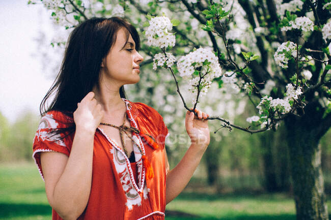Mujer en vestido rojo oliendo flores blancas - foto de stock
