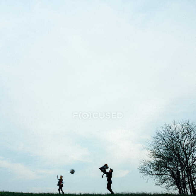 Отец играет с двумя детьми и воздушным шаром на холме — стоковое фото
