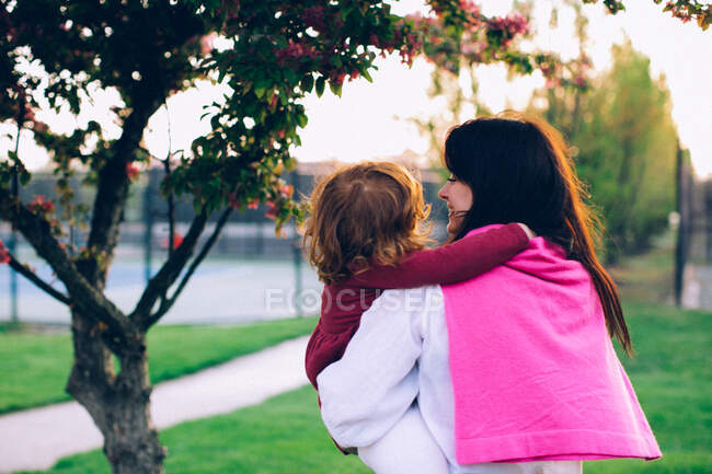 Woman holding her daughter under the tree and smiling — Stock Photo