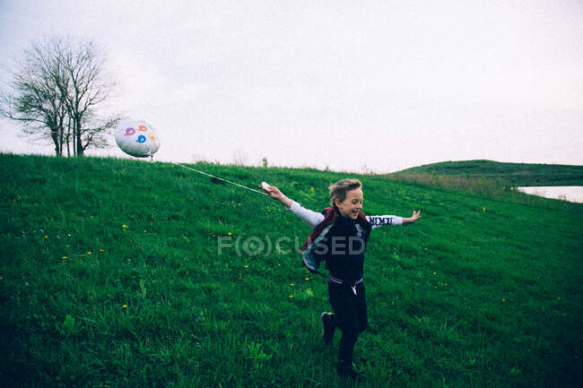 Хлопчик біжить з кулею на зеленому пагорбі — стокове фото
