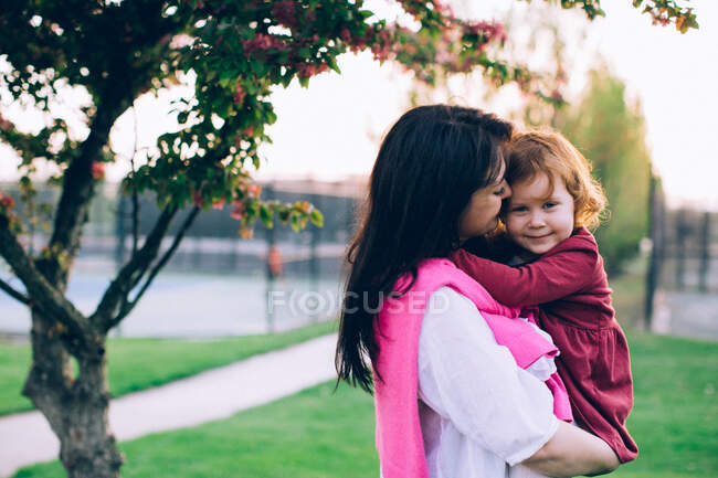 Femme tenant sa fille sous l'arbre et souriant — Photo de stock