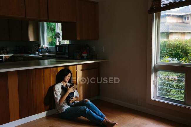 Madre sosteniendo a su hijo y sentada en la cocina - foto de stock